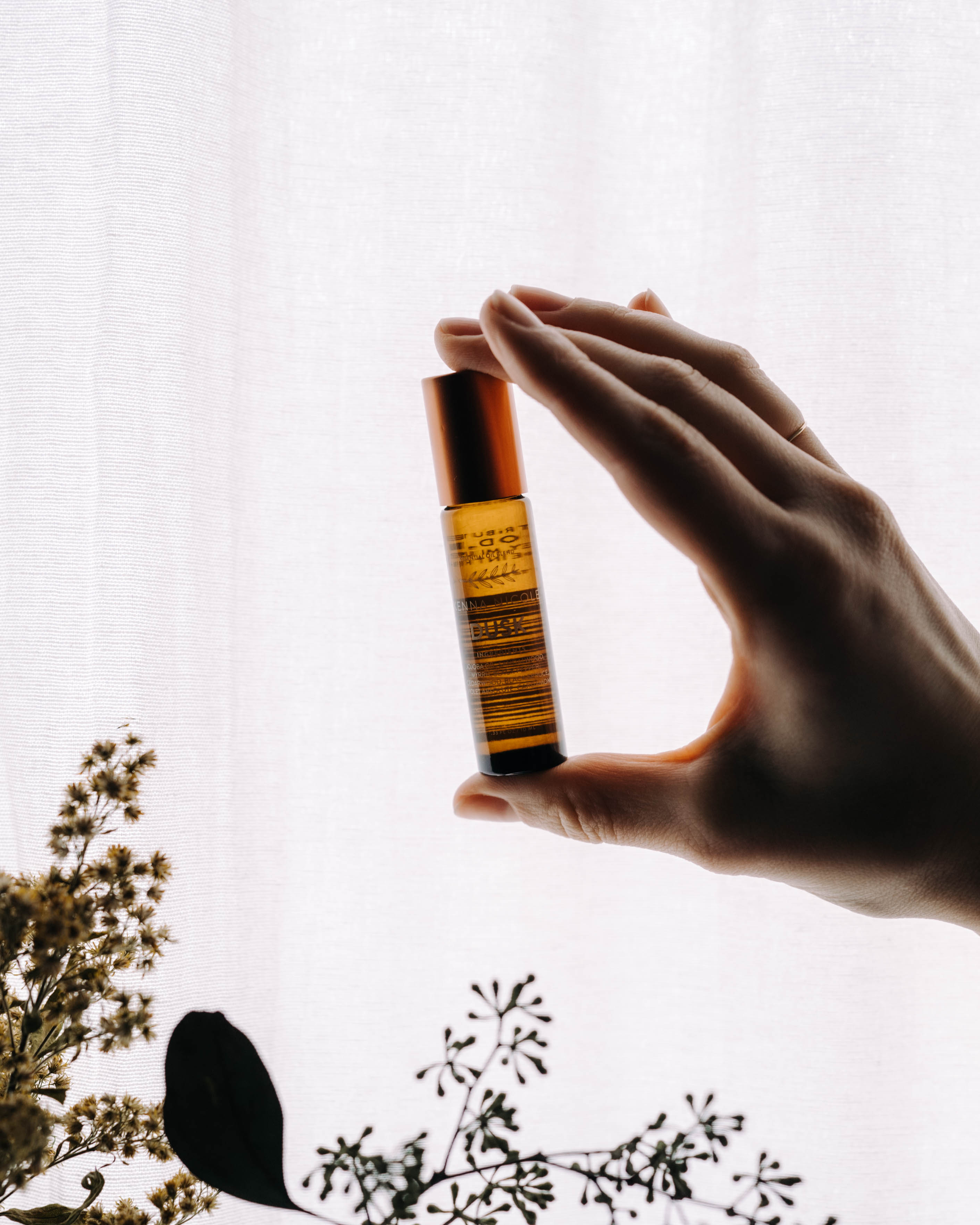 A hand holding dusk essential oil blend on a white sunlit background