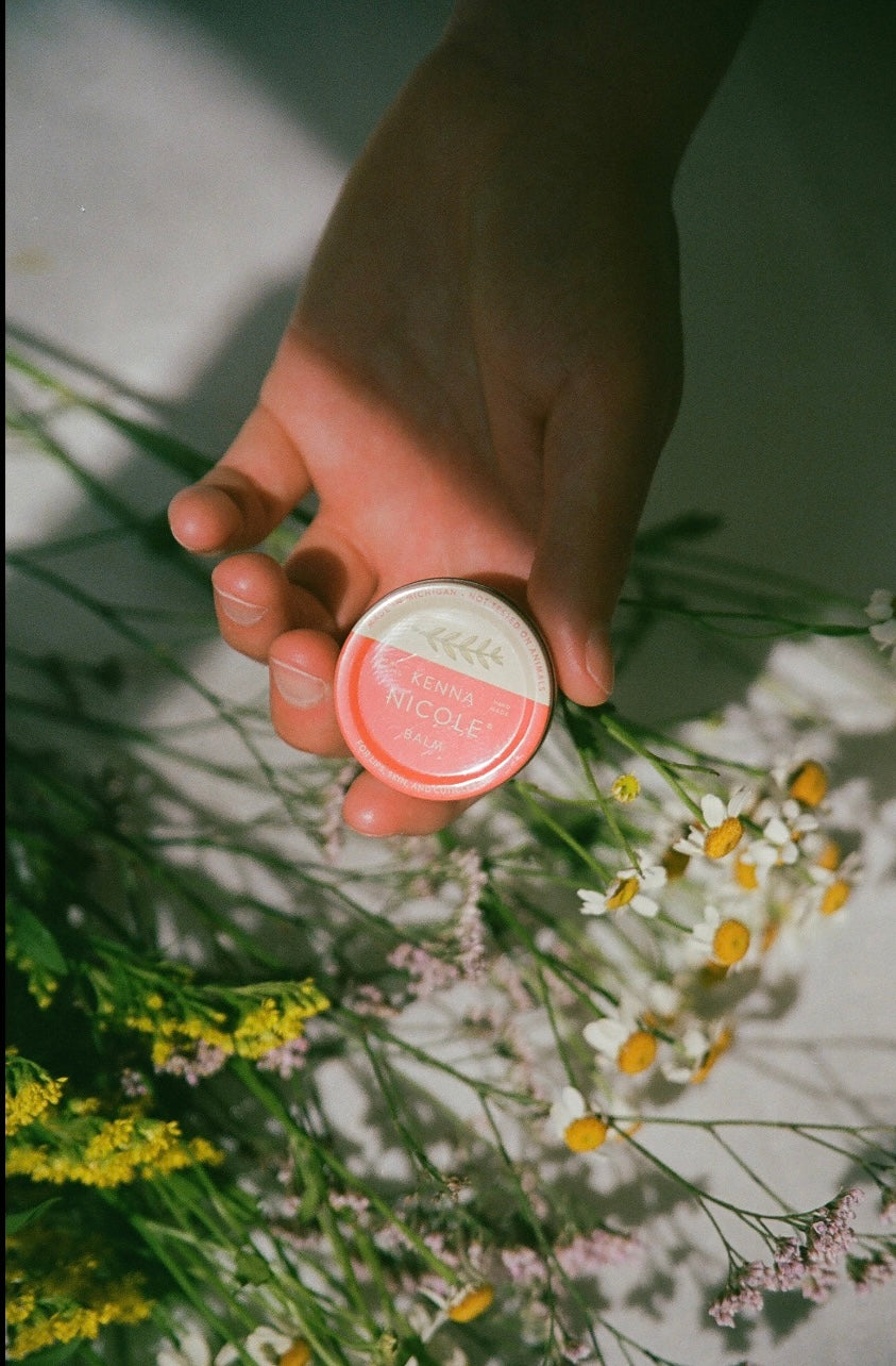 Hand holding a small container with flowers in the background