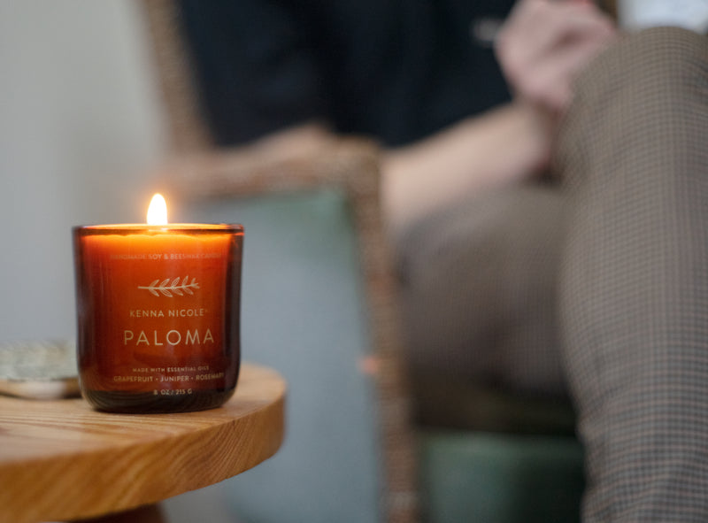 A Kenna Nicole candle burning on a wooden table